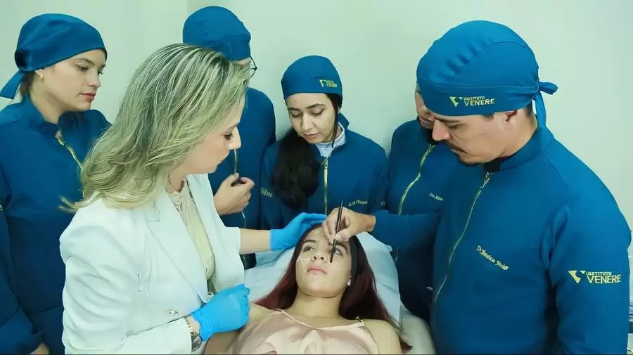 Alunos de touca e jaleco acompanhando procedimento em paciente